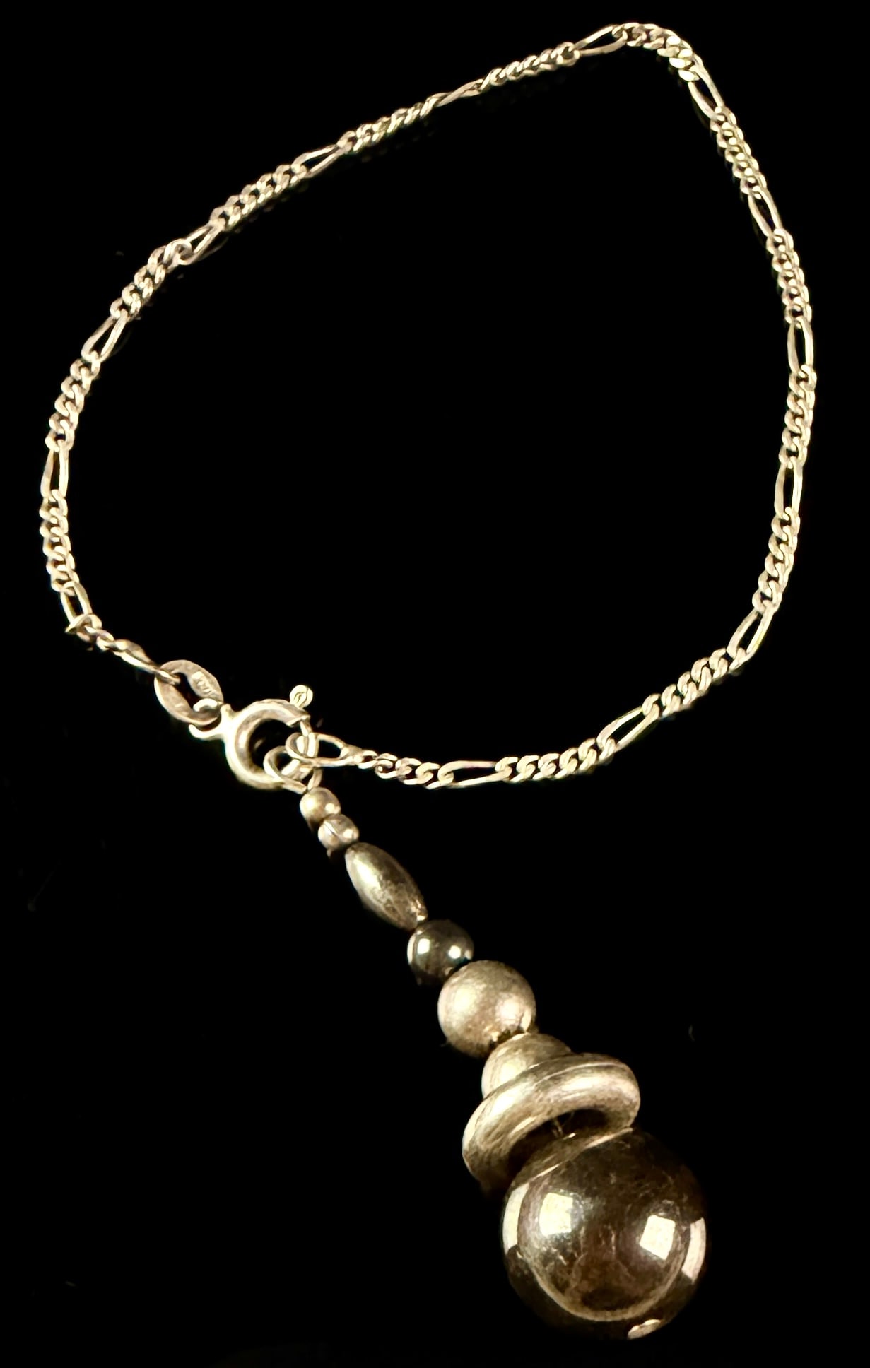 Italian Sterling Silver Figaro Chain Bracelet with Graduated Bead Drop: An Italian sterling silver bracelet featuring a Figaro link chain and a graduated bead pendant drop. The chain is constructed with a repeating pattern of three short circular links and one long oval l