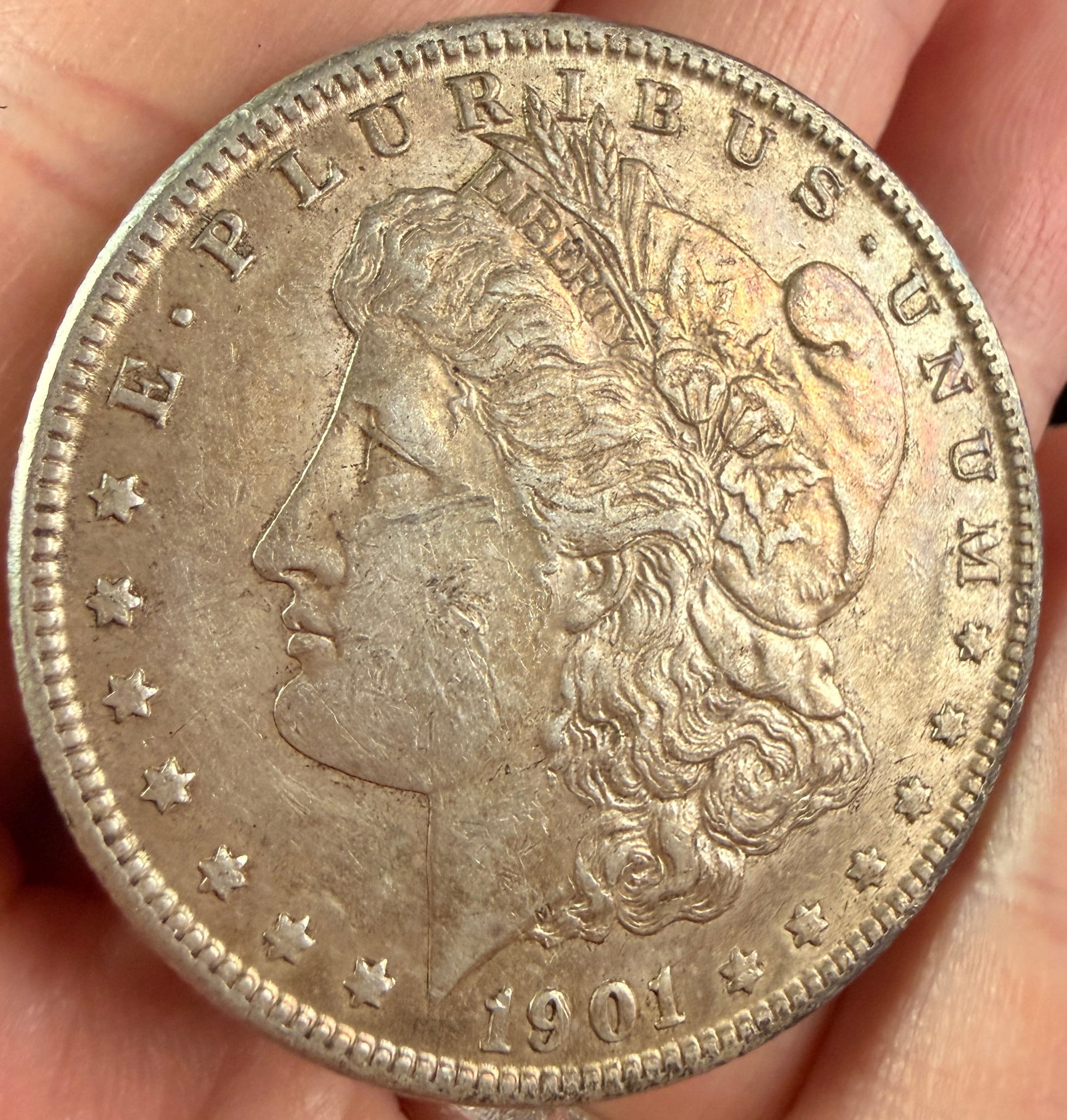 1901-O US Morgan Silver Dollar: A 1901-O US Morgan silver dollar. The obverse features a left-facing profile of Lady Liberty wearing a Phrygian cap and a coronet inscribed with the word LIBERTY. The profile is surrounded by the mott