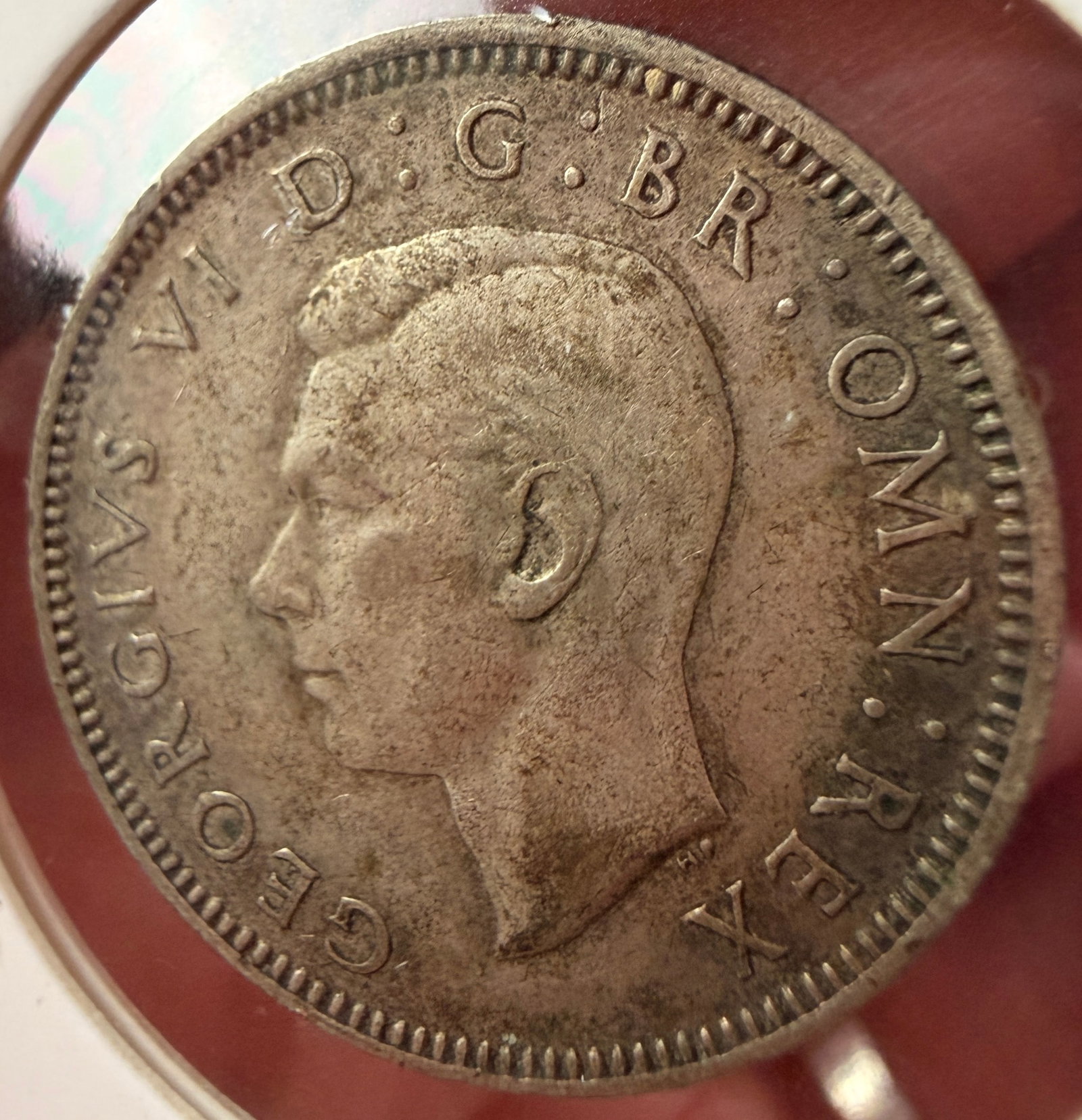 1942 UK George VI Silver One Shilling Coin: A 1942 United Kingdom silver one shilling coin struck in 0.500 silver. The obverse features the left-facing portrait of King George VI surrounded by the legend GEORGIVS VI D : G : BR : OMN : REX. A pa