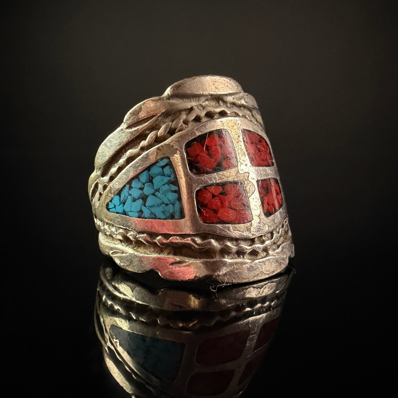 Southwestern Style Wide Band Ring with Turquoise and Coral Chip Inlay: A Southwestern style wide band ring constructed from an unmarked silver toned metal. The ring features a saddle style design with a central circular medallion divided into four recessed quadrants.