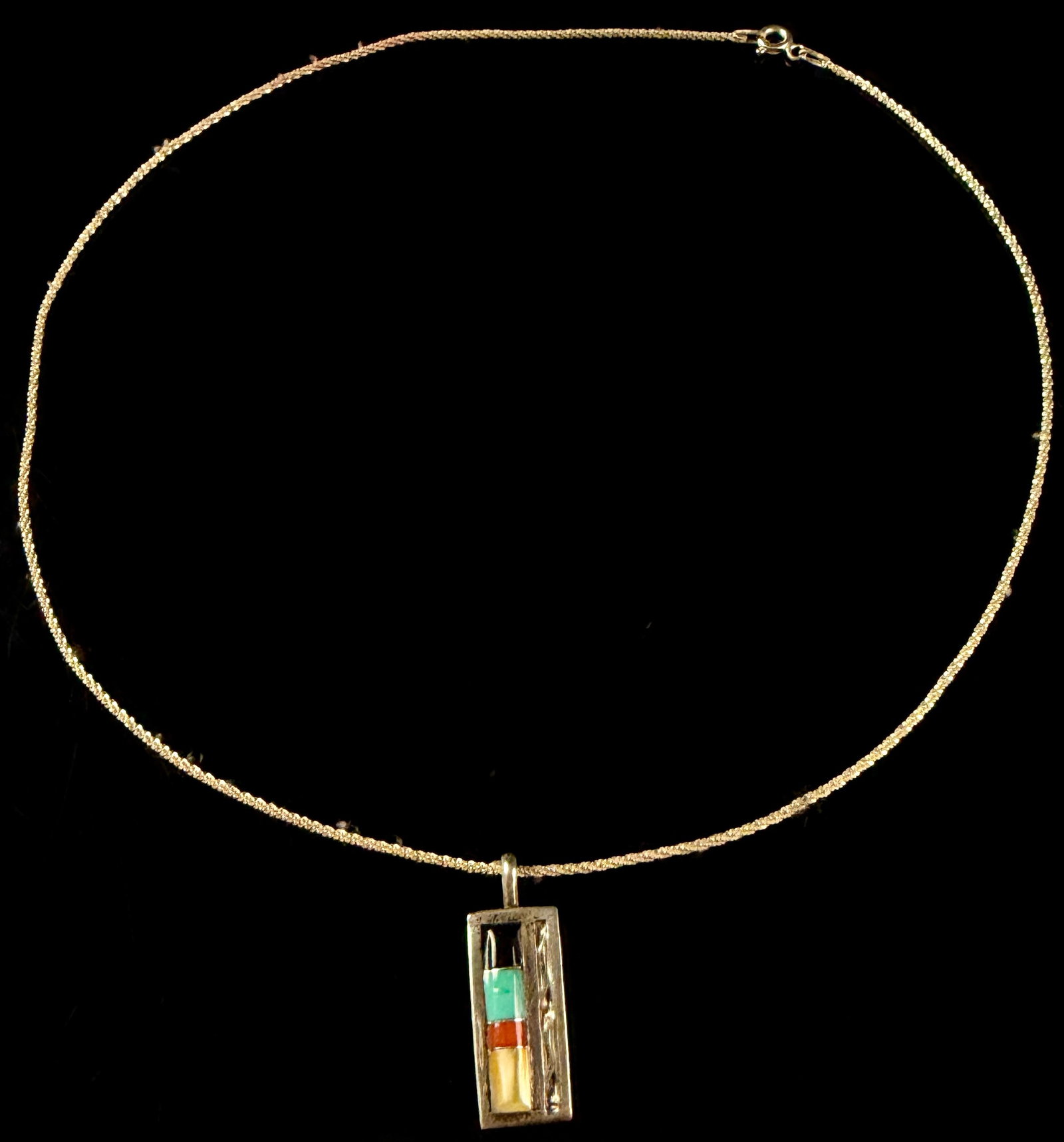 S & L Panteah Sterling Silver and Multi-Stone Inlay Pendant Necklace: An Italian sterling silver rope-link chain with a yellow gold wash supports a rectangular Zuni sterling silver pendant. The pendant features a channel-set vertical inlay of four stones: black jet,