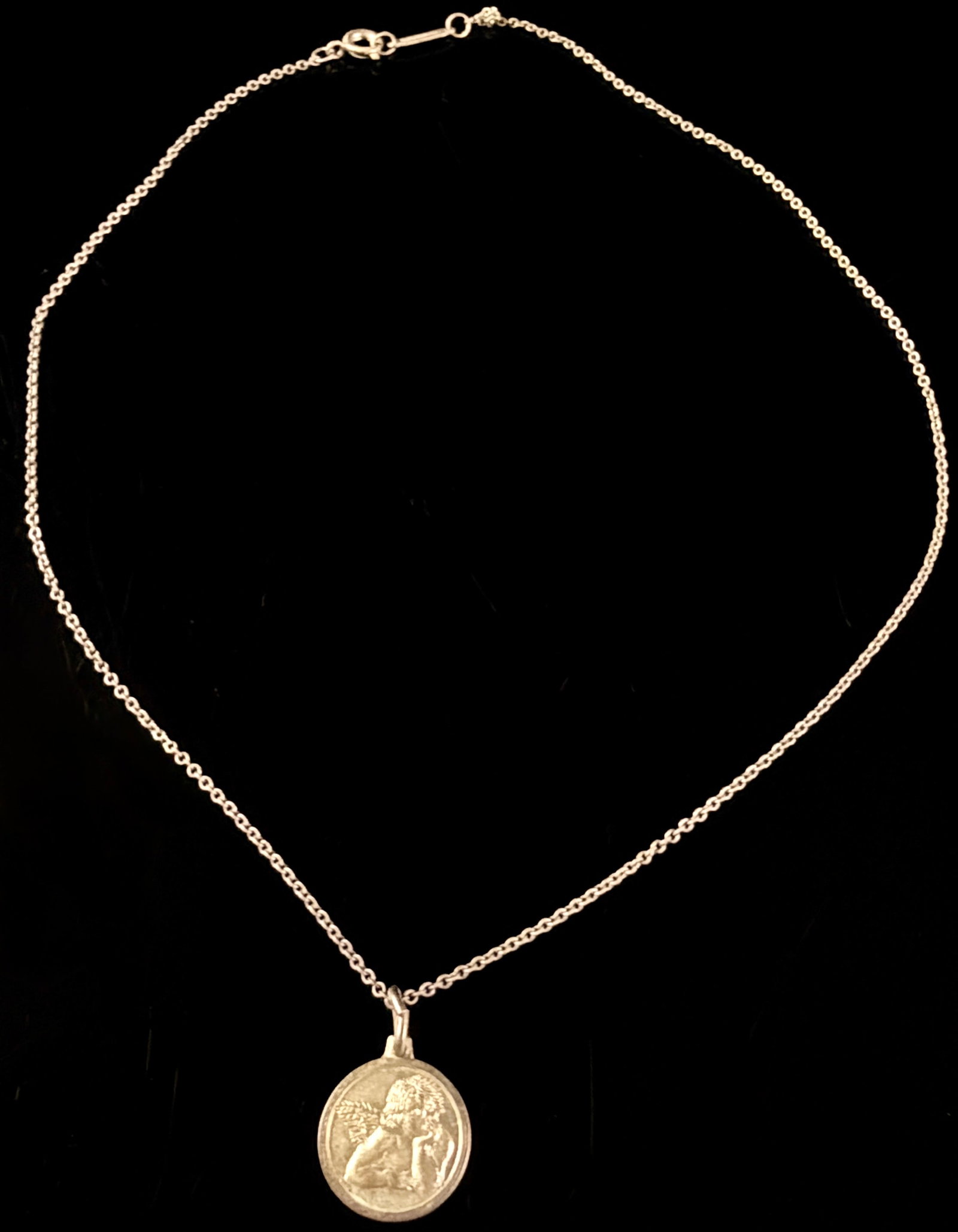 Tiffany & Co. Sterling Silver Cherub Pendant Necklace: An Italian Tiffany & Co. sterling silver necklace featuring a circular pendant with a relief depiction of a cherub resting its chin on its hand. The motif is derived from the angels in Raphael's
