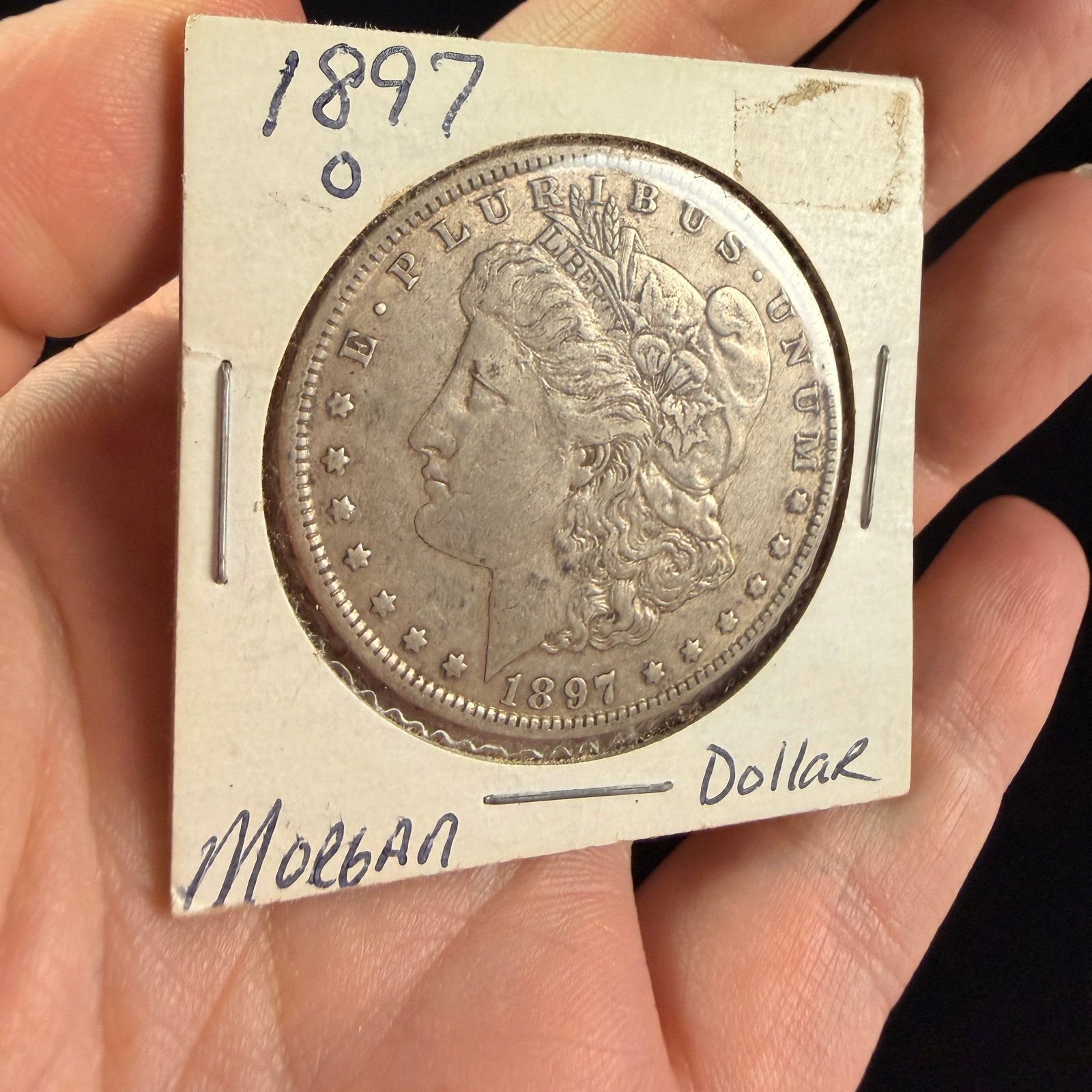 1897-O Morgan Silver Dollar: A US 1897-O Morgan silver dollar struck at the New Orleans Mint. The coin is composed of 90% silver and 10% copper with an actual silver weight of 0.7734 oz. The obverse features the Morgan design and