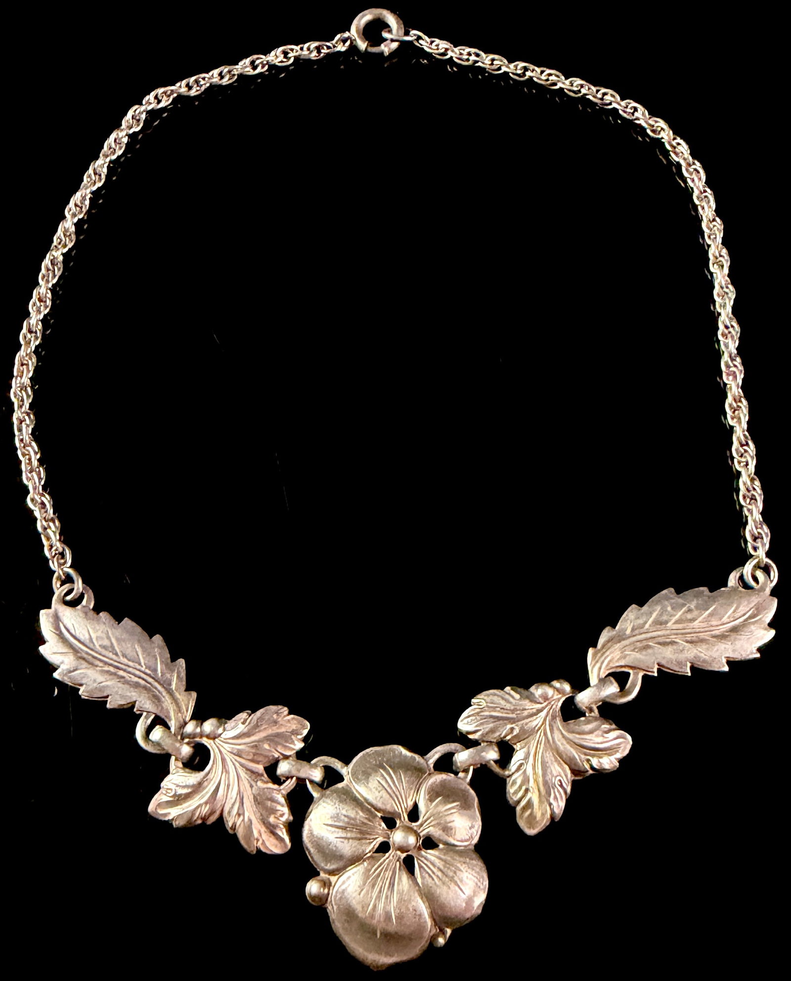 Sterling Silver Floral Festoon Necklace: A sterling silver necklace designed in a floral festoon style, featuring a central five-petaled flower element flanked by four foliate links. The decorative floral and leaf components are created