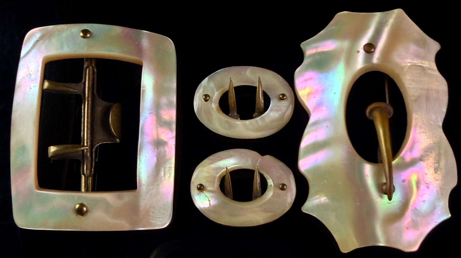 A Collection of Four Victorian Era Mother-of-Pearl Belt Buckles and Slides: This collection consists of four antique fashion accessories crafted from iridescent mother-of-pearl shell and brass-tone metal hardware. The shell exhibits natural nacreous luster with pink and