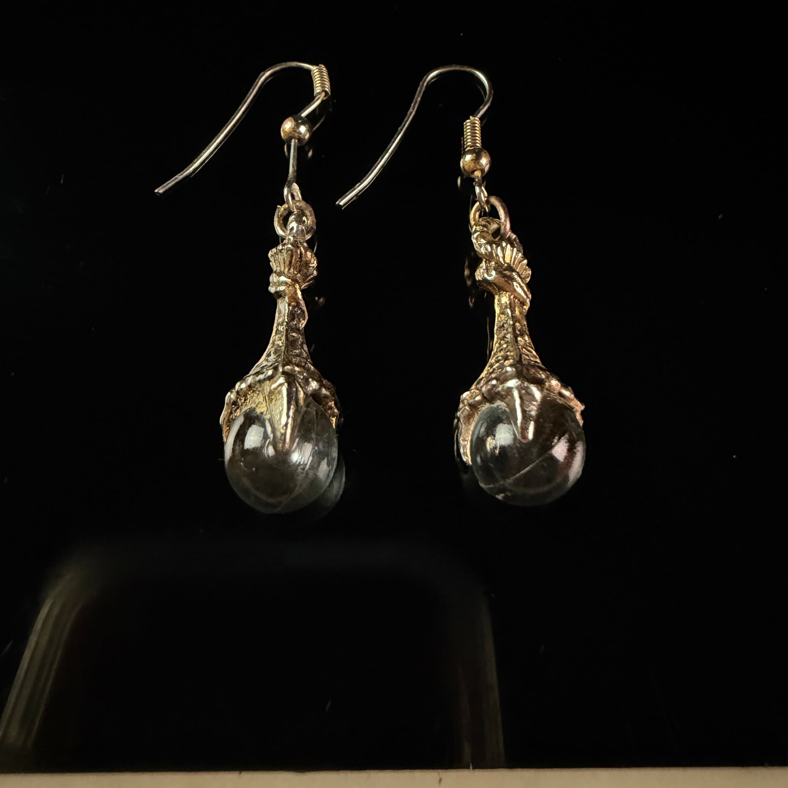 A Pair of Gothic Style Silver Tone Dragon Claw and Crystal Ball Drop Earrings: A matched pair of drop earrings for pierced ears. Each earring features a textured metal casting in the form of a bird of prey's talon or dragon's claw clutching a clear, colorless spherical orb. The 