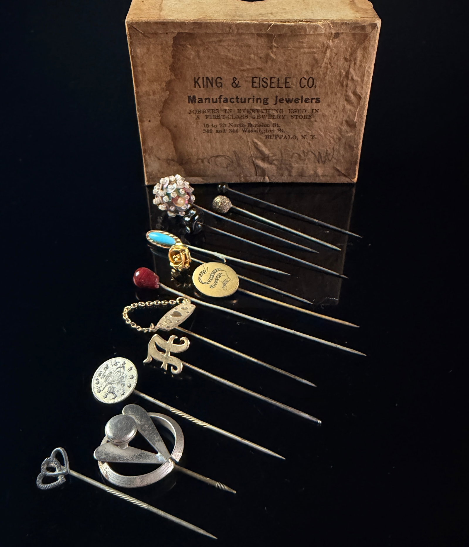 A Collection of Thirteen Antique and Vintage Stick Pins with King and Eisele Co. Box: A collection of thirteen antique and vintage stick pins of mixed styles and materials, housed in an original retailer box from Buffalo, New York. The assortment features a variety of motifs including 