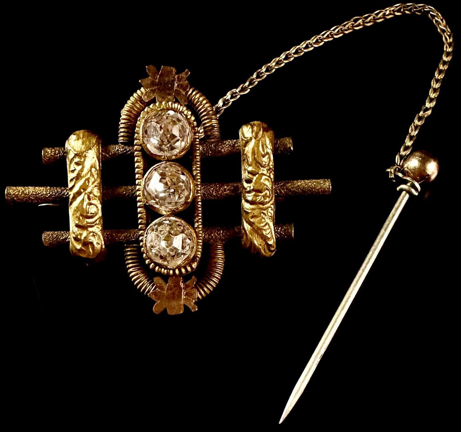 Victorian Bi-Color Gold and Three-Stone Bar Brooch with Safety Chain and Stick Pin: An antique Victorian-period bar brooch featuring a complex geometric design. The central element consists of a vertical column set with three clear, round, faceted stones featuring high crowns and lar