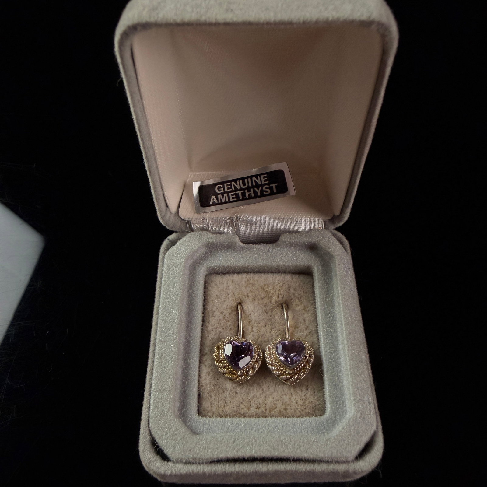 A Pair of Vintage Gold-Toned Amethyst Heart Drop Earrings with Original Ames Retail Packaging: A matched pair of heart-motif drop earrings featuring heart-cut purple gemstones. The stones are secured within yellow gold-toned settings with decorative rope-twist borders and are suspended from Fre