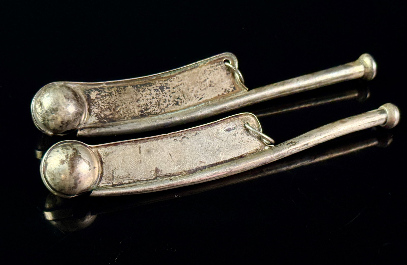 A Pair of Sterling Silver Boatswain Call Whistles: This lot features two nautical boatswain calls, also known as bosun whistles. Each piece is constructed with a narrow cylindrical pipe, a curved flat keel, and a spherical sound chamber called a buoy.