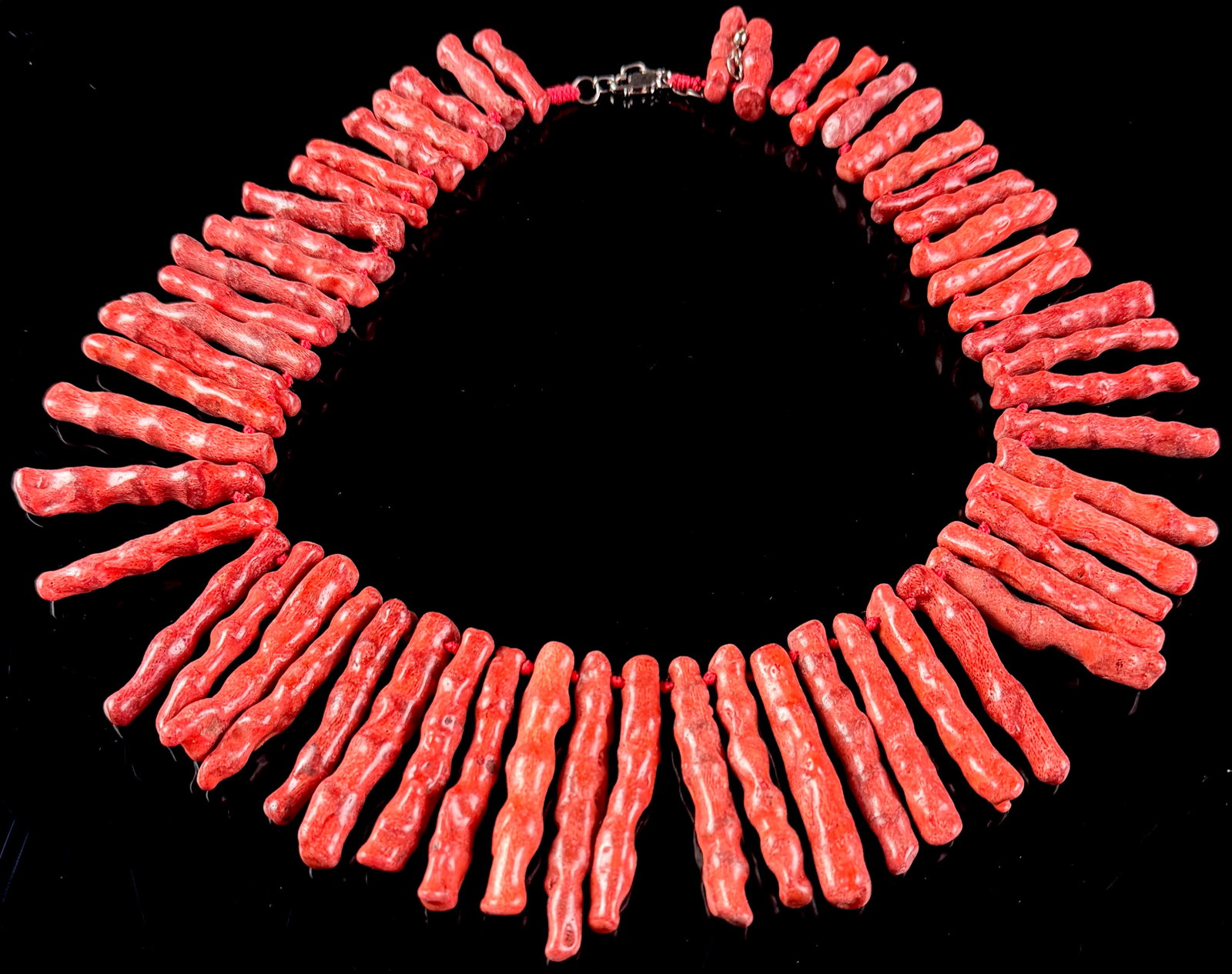 Graduated Red Branch Coral Fringe Necklace with Sterling Silver Clasp: A red branch coral fringe necklace featuring polished, graduated coral segments. The necklace is constructed on a red cord with individual knotted spacers positioned between each coral branch. The fas
