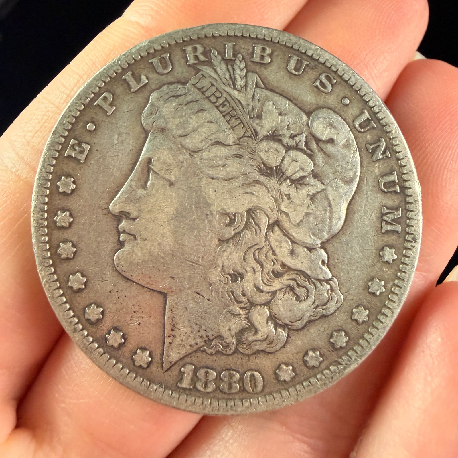 US 1880-O Morgan Silver Dollar: A US 1880 Morgan silver dollar composed of 90% silver and 10% copper with a reeded edge. The obverse features the Morgan design with thirteen stars and the date 1880. The reverse features a heraldic e