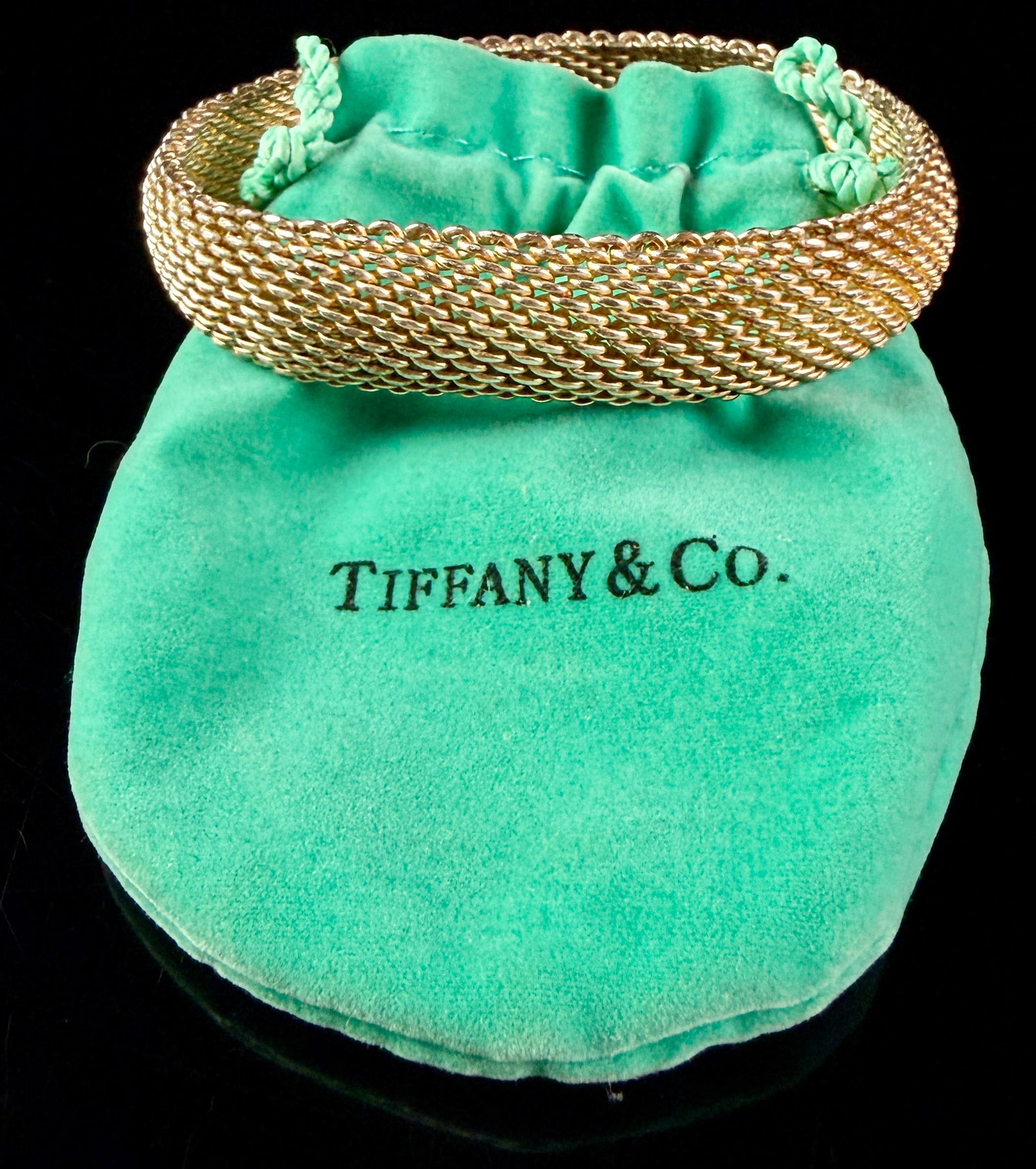 Tiffany and Co. Somerset Sterling Silver Mesh Bangle Bracelet: A circular bangle bracelet featuring a woven mesh design. The piece is constructed from sterling silver with a gold-toned finish. A raised hallmark tag on the interior is impressed with the text TIFFA