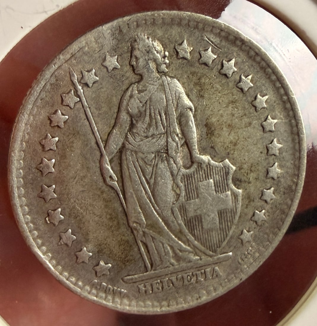 CH 1945 B 1 Franc Silver Coin: A 1945 silver 1 Franc coin from Switzerland, cataloged as KM# 24. The obverse displays the Standing Helvetia design type encircled by twenty-two stars. An impressed mark at the base reads HELVETIA and
