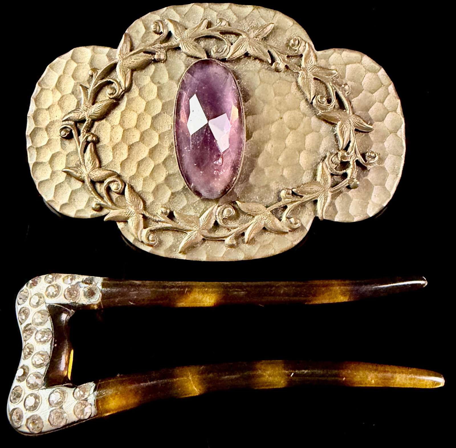 Two pieces of vintage costume jewelry comprising a hammered metal foliate sash brooch and a: A lot consisting of two items of costume jewelry. The first item is a large horizontal sash brooch of trilobed form, constructed from gold toned base metal. The design features a hammered honeycomb te