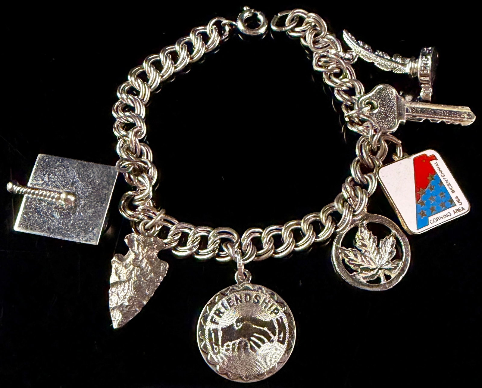 Sterling Silver Charm Bracelet with Danecraft and Wells Charms: A sterling silver double-link charm bracelet featuring an assortment of figural and commemorative charms. The chain is fitted with a spring ring clasp impressed with the word STERLING. One charm is mo