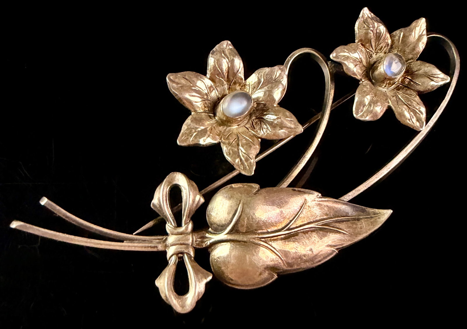 Sterling Silver and Moonstone Floral Spray Brooch: A vintage floral spray brooch crafted from sterling silver. The botanical motif features two six-petaled flowers, a single large ribbed leaf, and three stems gathered by a tied ribbon bow. Each flower