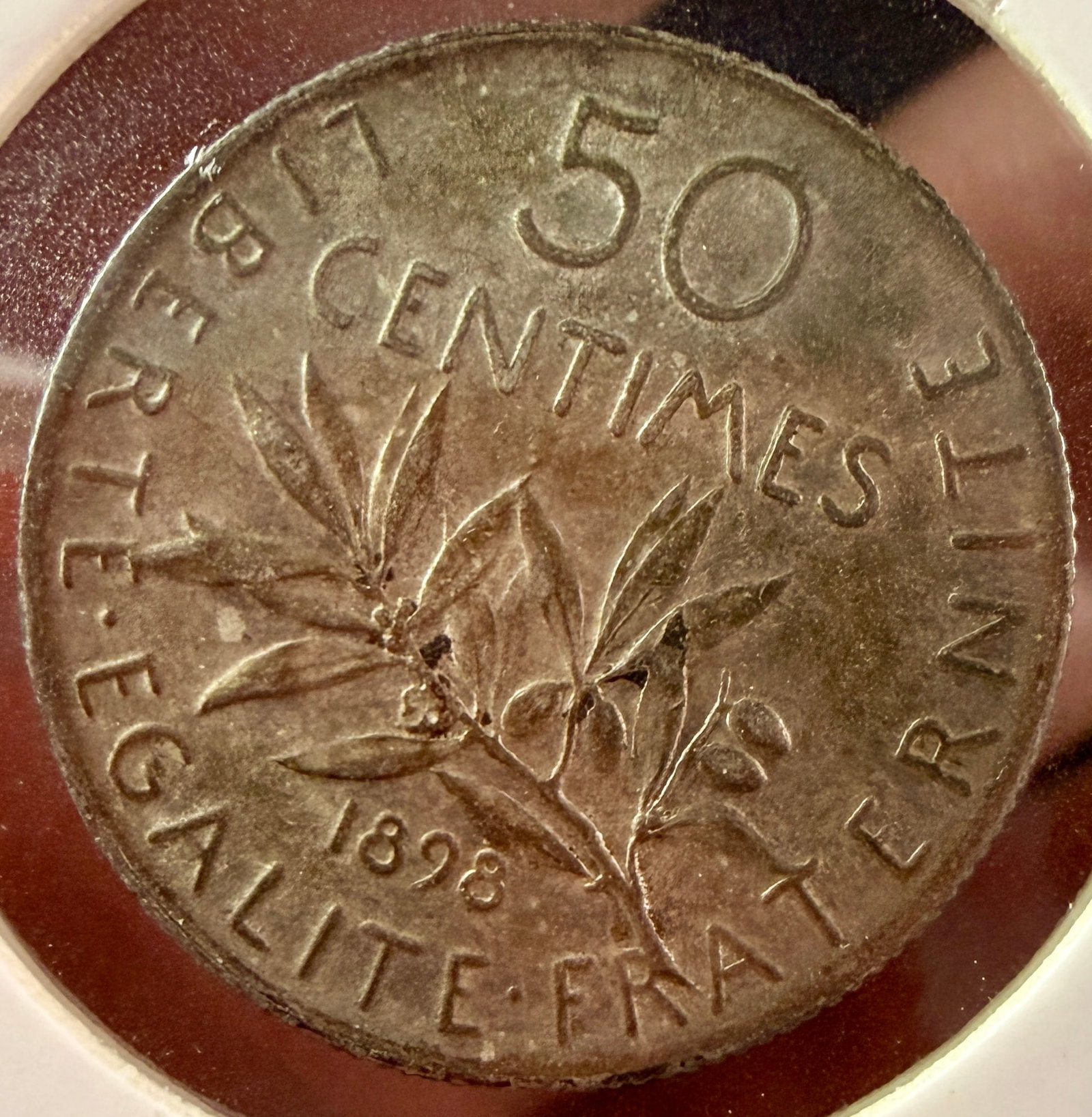 1898 FR Silver 50 Centimes Coin: This FR 50 Centimes silver coin was issued in 1898 by the French Republic. The obverse displays the Sower (La Semeuse) design with the legend REPUBLIQUE FRAN?‡AISE. The reverse features an olive bra