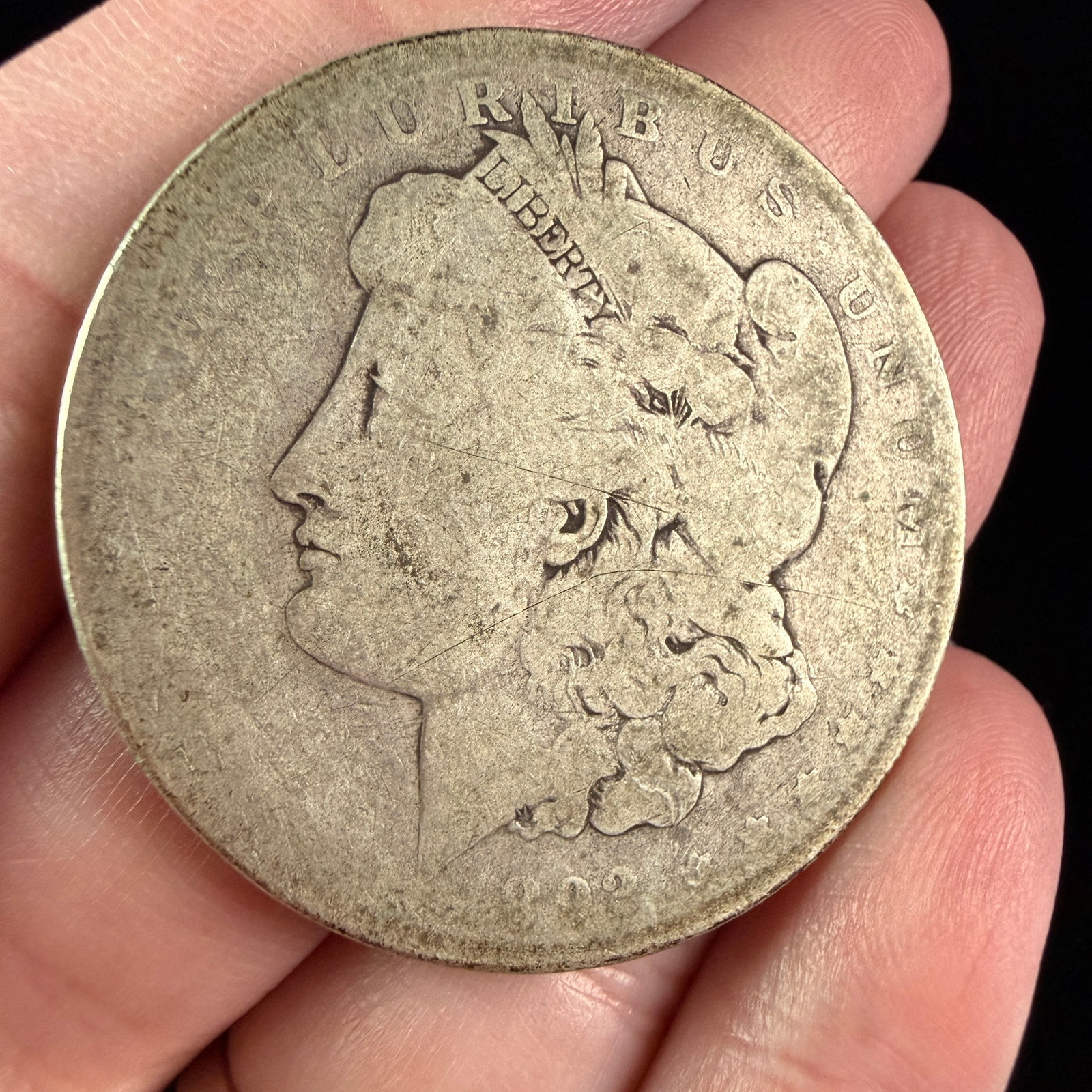 1898-O US Morgan Silver Dollar: A struck US 1898 Morgan Silver Dollar composed of silver-colored metal. The obverse is inscribed along the rim with the legend E PLURIBUS UNUM and the date 1898 at the bottom. The headband of the cent
