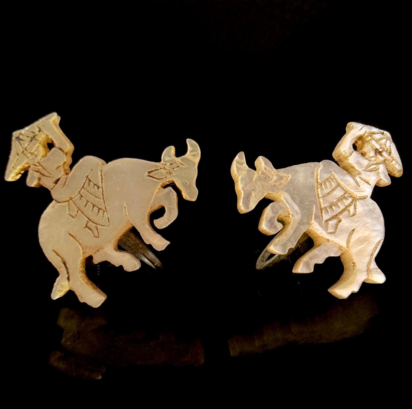 A Pair of Japanese Hand-Carved Mother-of-Pearl Water Buffalo Earrings: A matched pair of Japanese screw-back earrings featuring hand-carved folk art designs. Each earring is crafted from a single piece of iridescent mother-of-pearl, intricately carved to depict a figure
