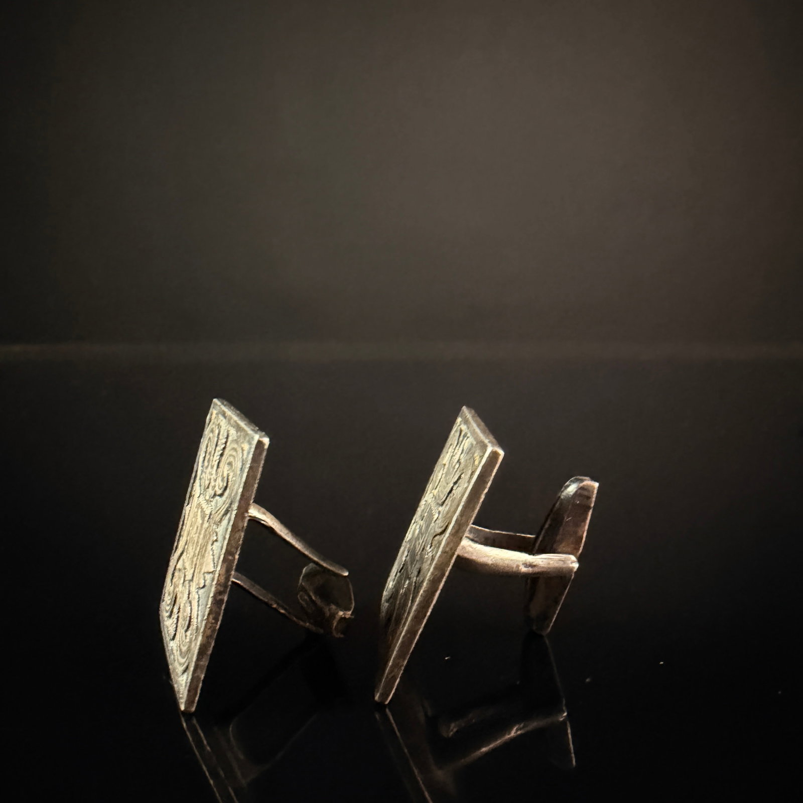 A Pair of Mexican Sterling Silver Square Scrollwork Cufflinks: A pair of Mexican sterling silver square cufflinks featuring a relief-cast scrolling foliate design. Each face contains a central square cartouche housing a stylized relief symbol. The cufflinks are