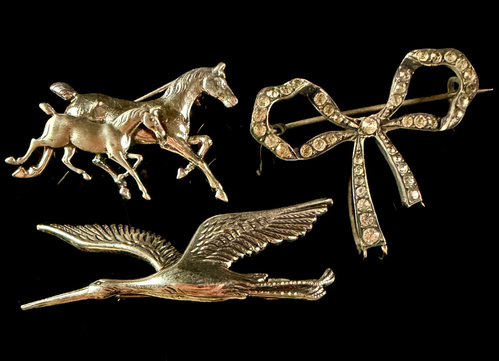A Trio of Vintage Sterling Silver Brooches Including Horse and Bird Motifs: This lot consists of three vintage sterling silver brooches with various decorative and figurative themes. The first brooch depicts a mare and foal in mid-gallop with textured finishes. The reverse