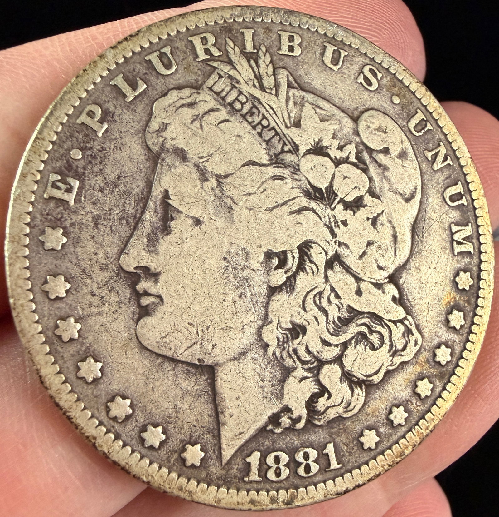 US 1881-O Morgan Silver Dollar: A US silver dollar, Morgan type, dated 1881. This coin was struck at the New Orleans Mint, identified by an impressed letter O mint mark located on the reverse, centered above the DO in DOLLAR. The