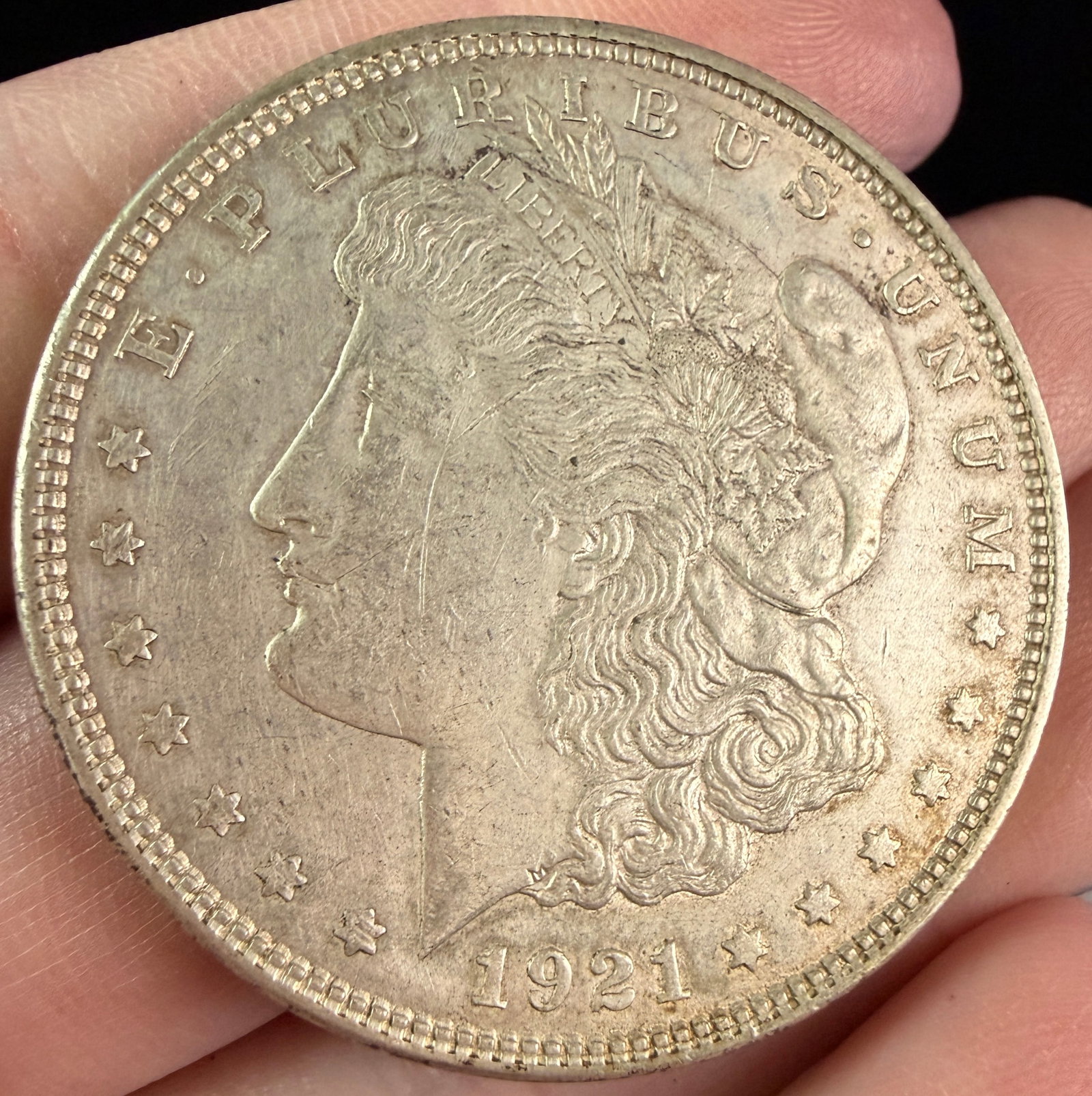 US 1921 Morgan Silver Dollar: A US 1921 Morgan silver dollar struck at the Philadelphia Mint. This silver coin features the Liberty head obverse and the eagle and wreath reverse. No mint mark is present. The coin has a reeded