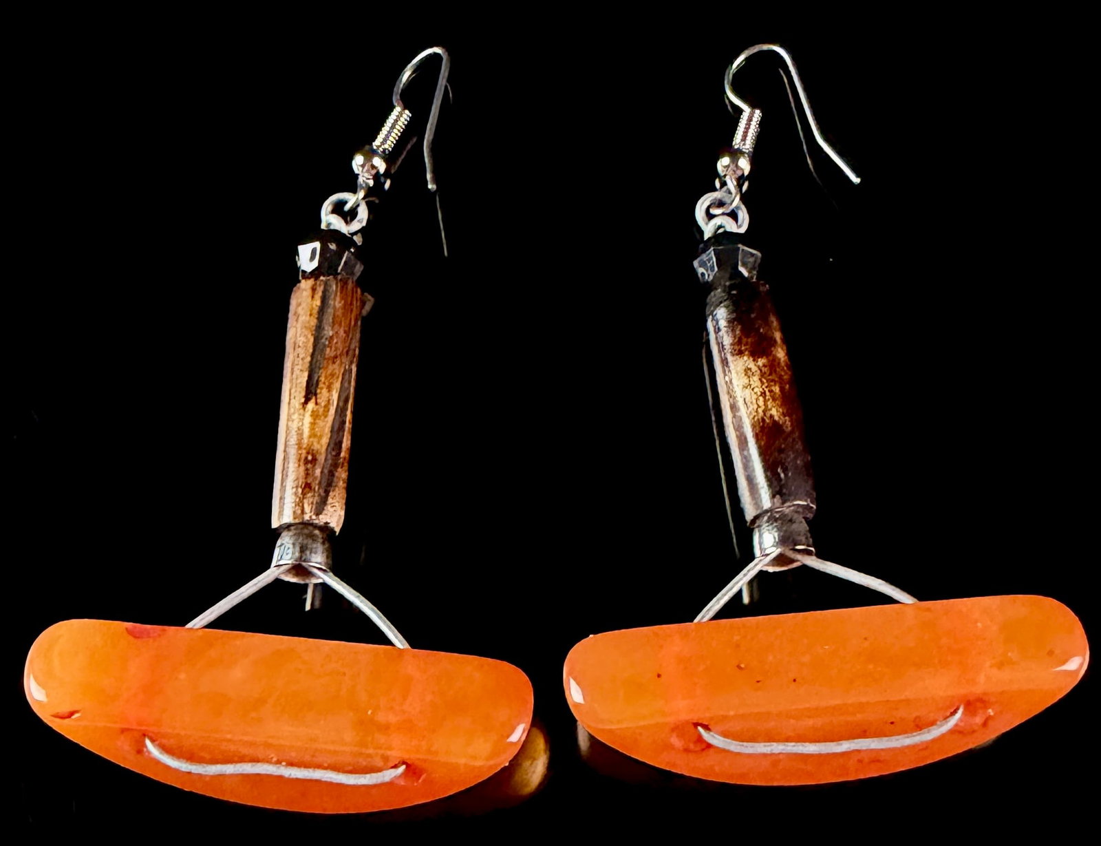 A Pair of Catalan Amber and Mixed Media Statement Drop Earrings: A matched pair of artisanal drop earrings featuring large semi-circular elements of polished, semi-translucent orange Catalan amber. The amber sections are suspended by silver-tone wire frames from