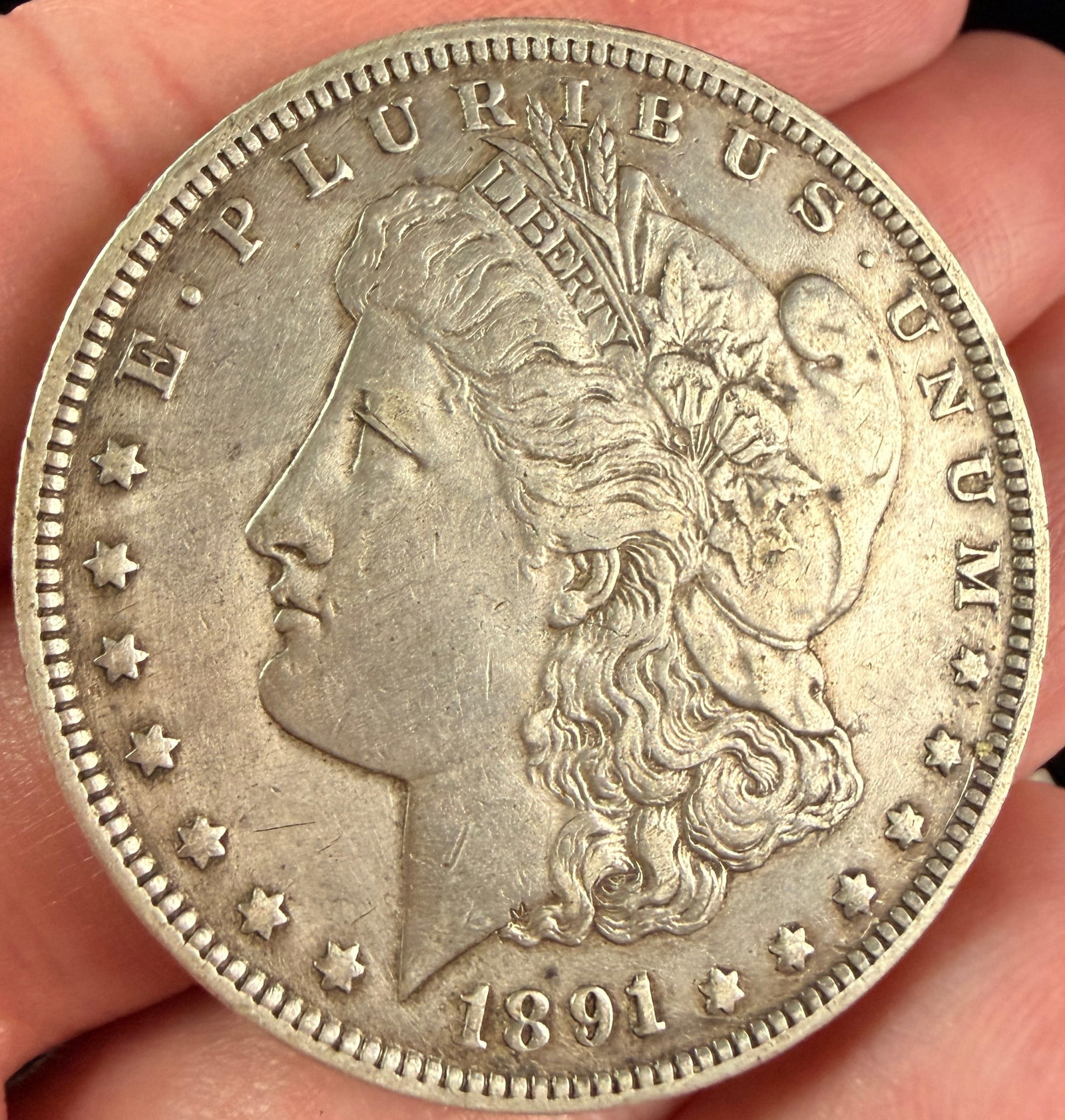 US 1891-O Morgan Silver Dollar: A US Morgan silver dollar struck at the New Orleans mint. The obverse features a profile of Liberty facing left, wearing a Phrygian cap, with the date 1891 at the base and the legend E PLURIBUS UNUM