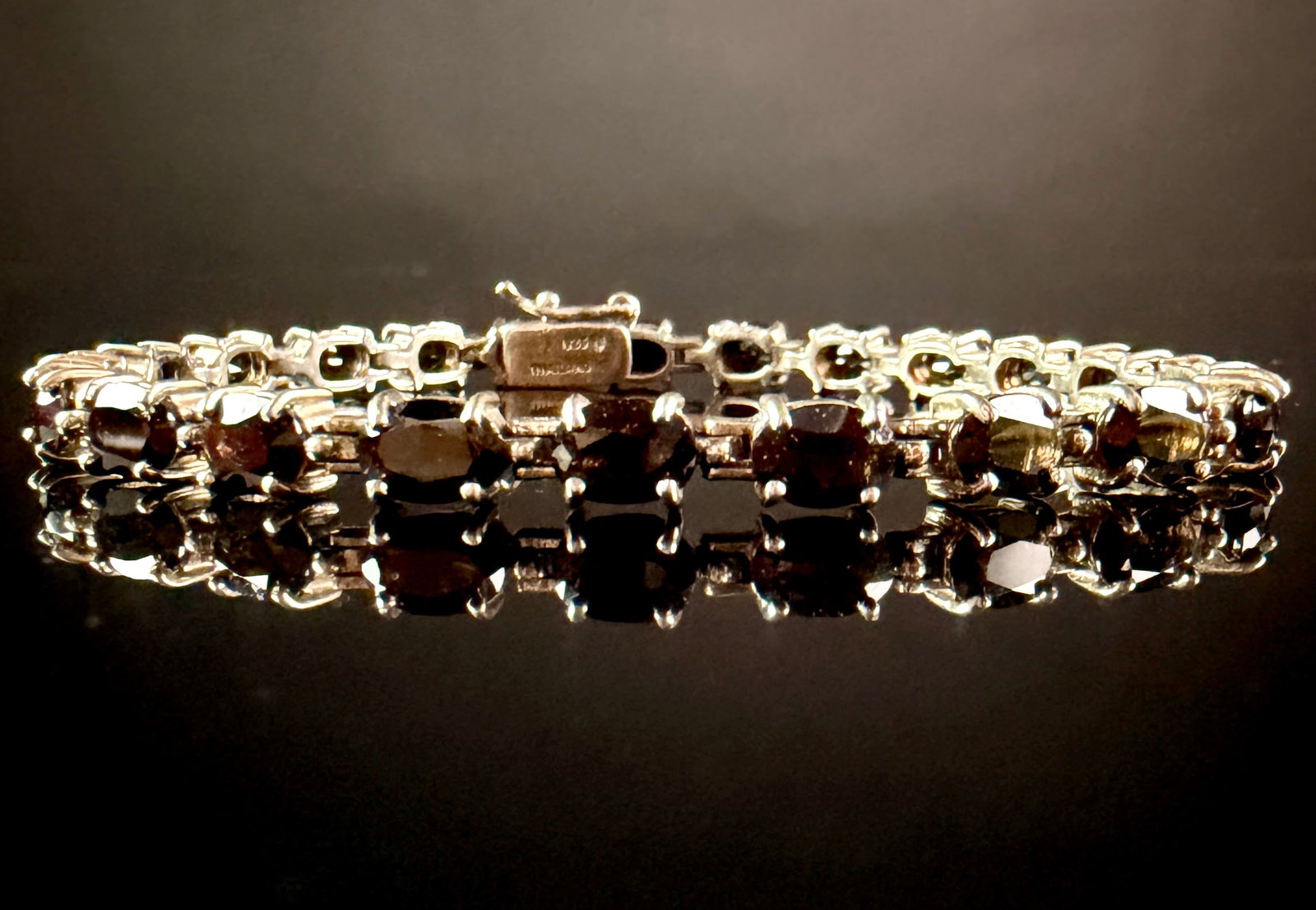 Sterling Silver and Oval-Cut Garnet Tennis Bracelet: A sterling silver tennis link bracelet featuring a continuous row of approximately 30 prong-set, oval-cut garnets. Each dark burgundy-red gemstone is secured in a four-prong mounting. The articulated 