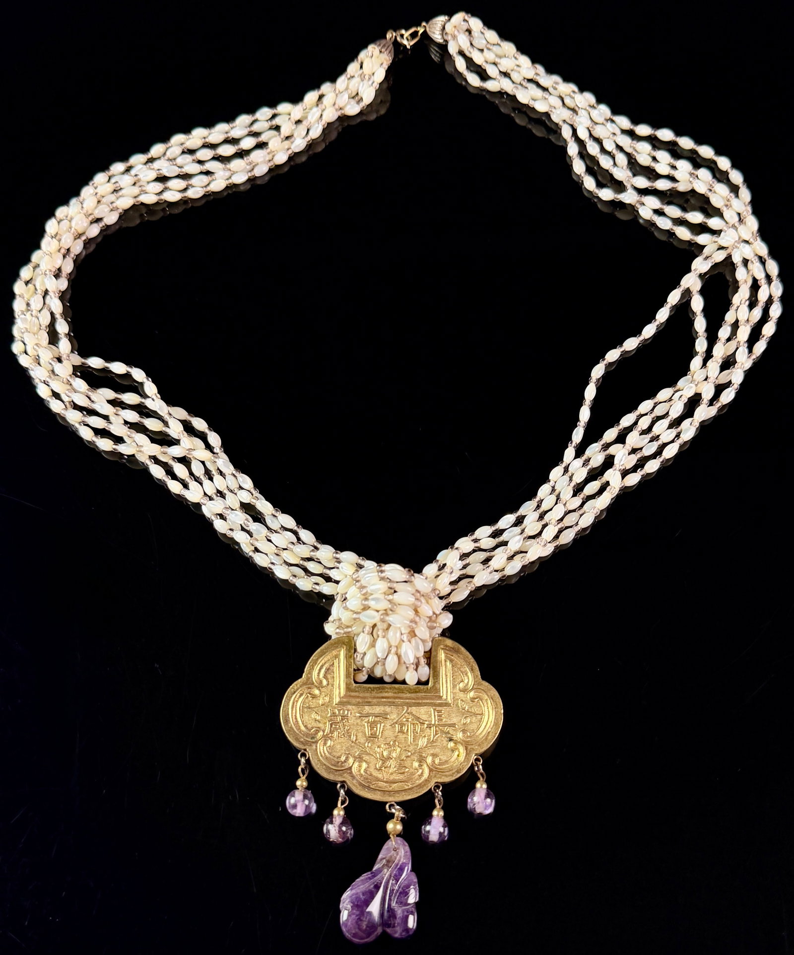 A Multi-Strand Mother-of-Pearl and Amethyst Longevity Lock Whistle Necklace: A multi-strand necklace composed of six strands of mother-of-pearl rice beads interspersed with small purple glass spacers. The strands are gathered into a knotted bead cluster above a gold-filled Ruy