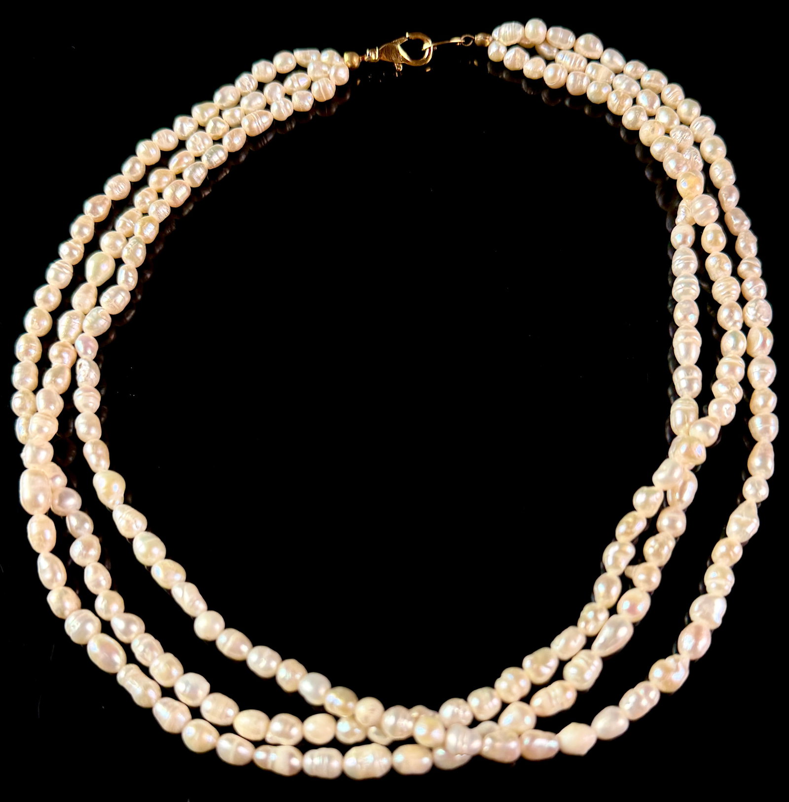 Triple-Strand Freshwater Rice Pearl Necklace with Yellow Metal Lobster Claw Clasp: A triple-strand necklace featuring creamy-white freshwater pearls. The pearls are baroque in form, specifically a rice shape with characteristic horizontal surface ridges and natural surface irregular