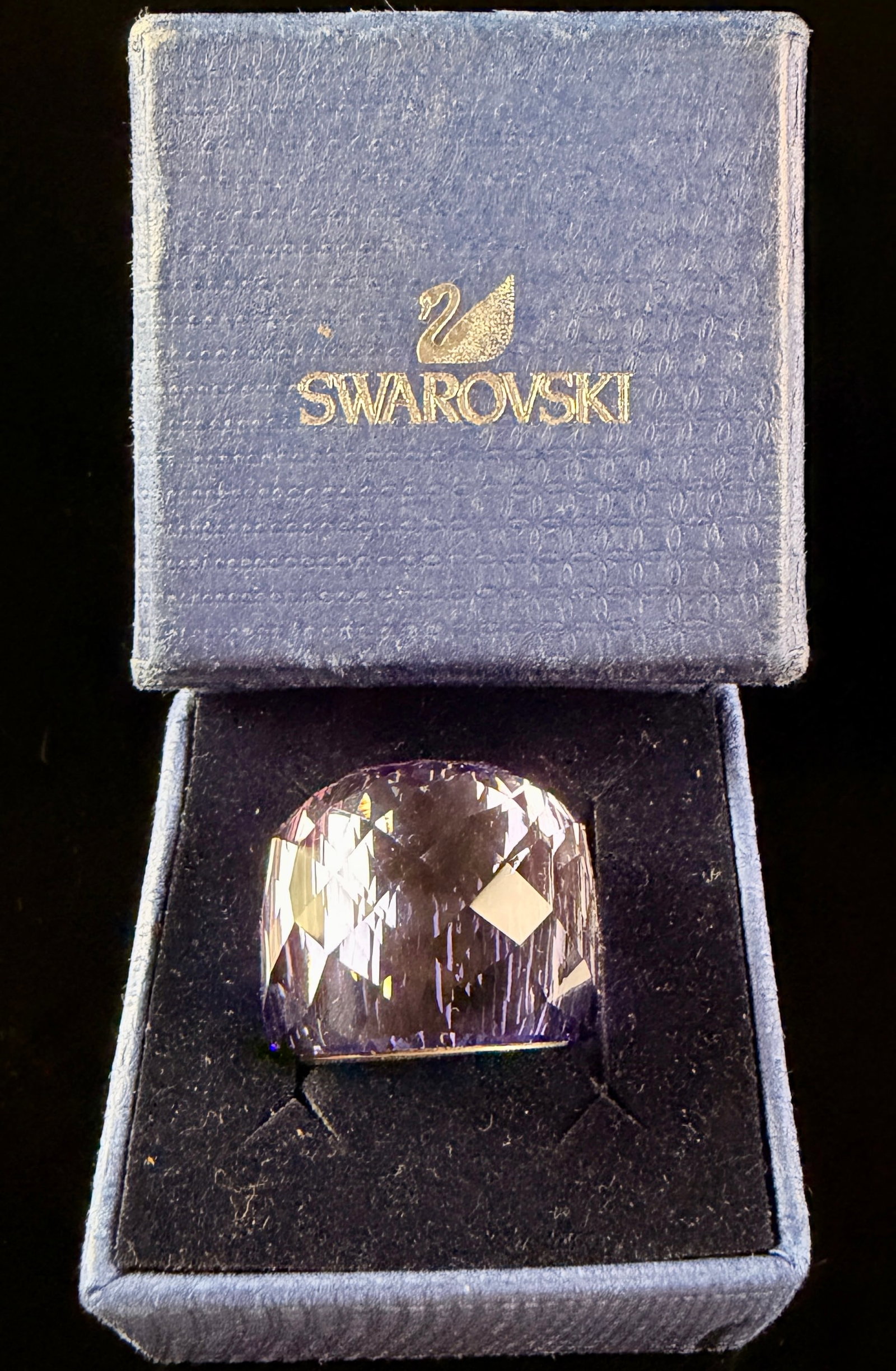 Swarovski Nirvana Purple Crystal Cocktail Ring Size 52 with Presentation Box: A Swarovski cocktail ring in the Nirvana design, featuring a large, faceted violet crystal exterior bonded to a polished silver-tone metal inner sleeve. The chunky crystal body is cut with numerous fa