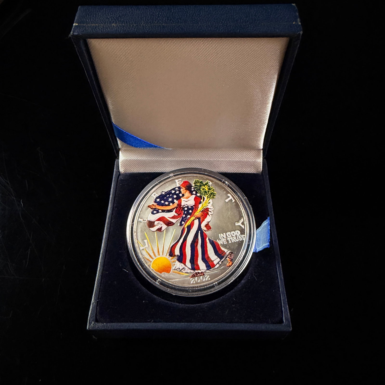 2002 US Colorized American Silver Eagle One Dollar Coin: This 2002 US American Silver Eagle one dollar coin is composed of 1 oz of .999 fine silver and features an aftermarket colorized finish on the obverse. The coin is housed in a clear protective plastic