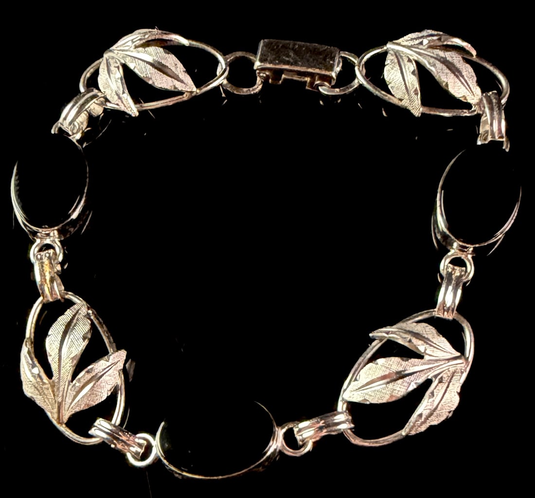 A&Z Sterling Silver and Black Onyx Leaf Link Bracelet: This vintage link bracelet is crafted from sterling silver and features four oval black onyx cabochons in bezel settings. These links alternate with four botanical motif links, each depicting three te