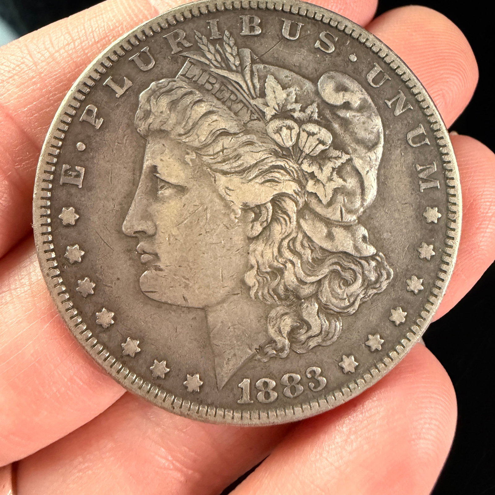 1883 US Morgan Silver Dollar: A United States 1883 Morgan silver dollar, produced at the Philadelphia Mint as indicated by the absence of a mint mark. The coin features the obverse design by George T. Morgan, showing a left-facing