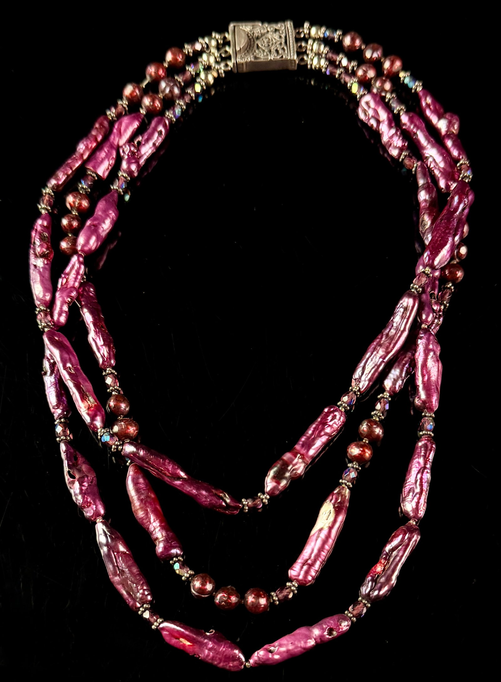 Triple-Strand Magenta Dyed Freshwater Pearl and Glass Bead Necklace with Sterling Silver Clasp: A triple-strand necklace featuring elongated stick pearls and round pearls, all dyed a vibrant metallic magenta. The strands are interspersed with faceted purple glass beads, some with an iridescent a