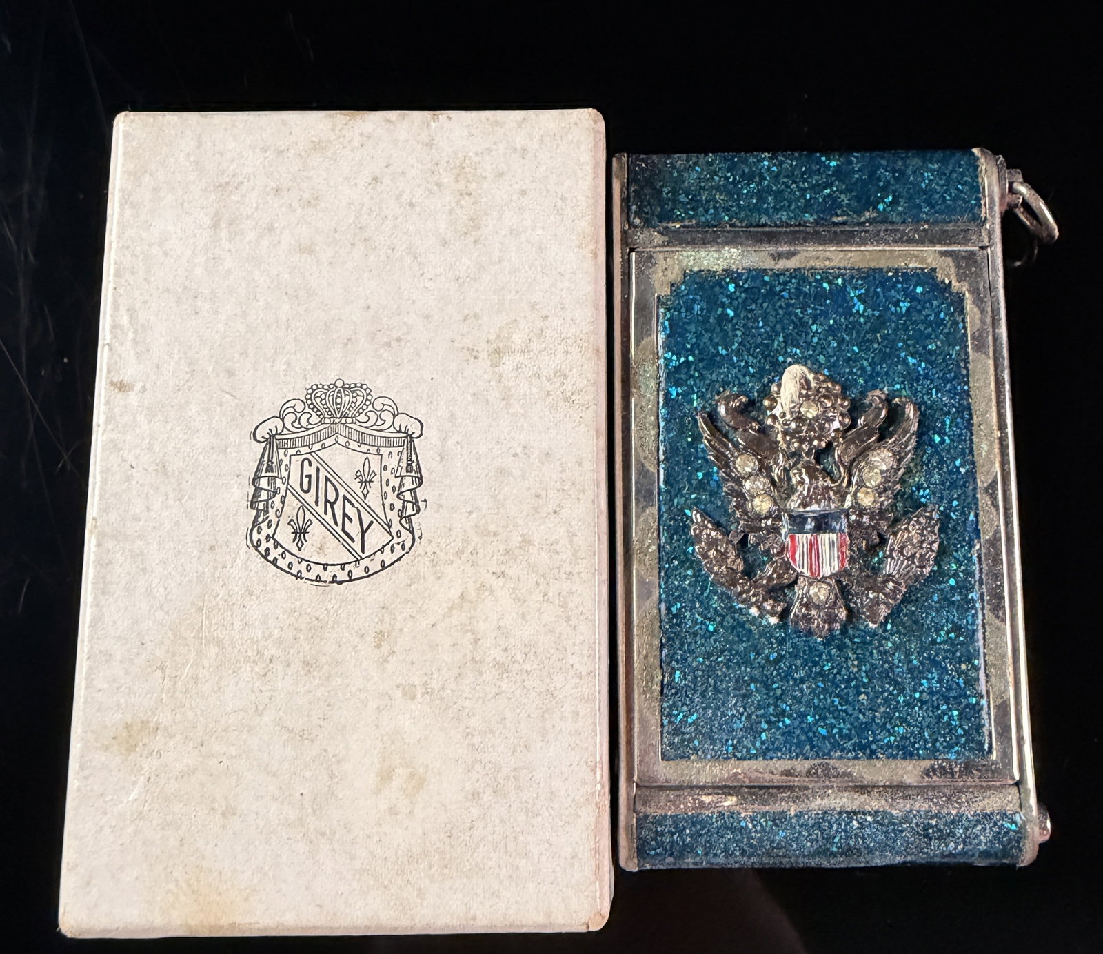 Girey World War II US Military Sweetheart Vanity Compact in Original Box: A mid-20th century American dual-compartment vanity compact manufactured by Girey. The rectangular silver-toned metal case features turquoise-blue crushed stone inlay on the front and back faces. An a