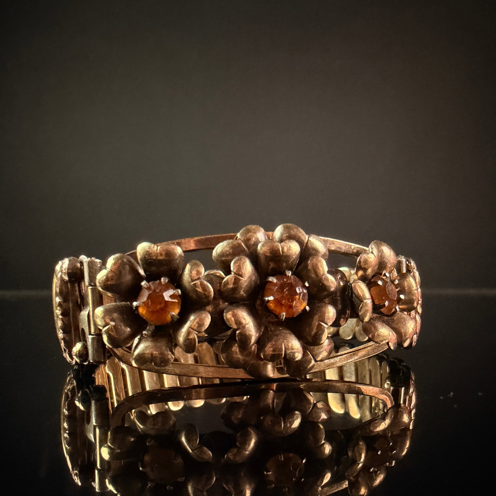 Lustern 12 Karat Gold Filled over Sterling Silver Floral Expansion Bracelet: A vintage expansion-link bracelet featuring a decorative floral centerpiece. The central panel is adorned with three stylized blossoms, each prong-set with a faceted round amber-colored stone. The ban