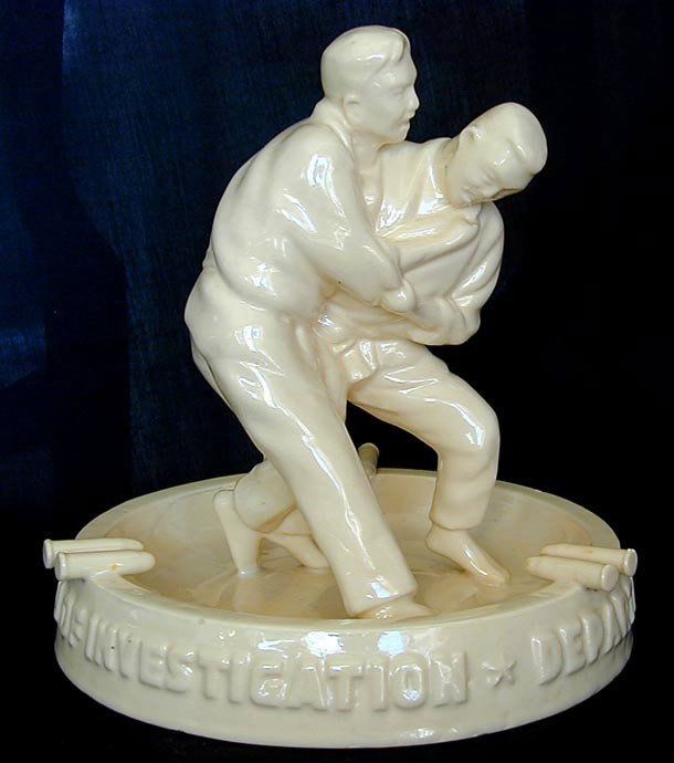 CIRCA 1940S DEPT OF JUSTICE NATIONAL BUREAU OF INV: A vintage yellow pottery figural ashtray w/ 2 men practicing the martial arts and pairs of ceramic bullets for the cigar or cigarette holders, molded with the titles Department of Justice & National B