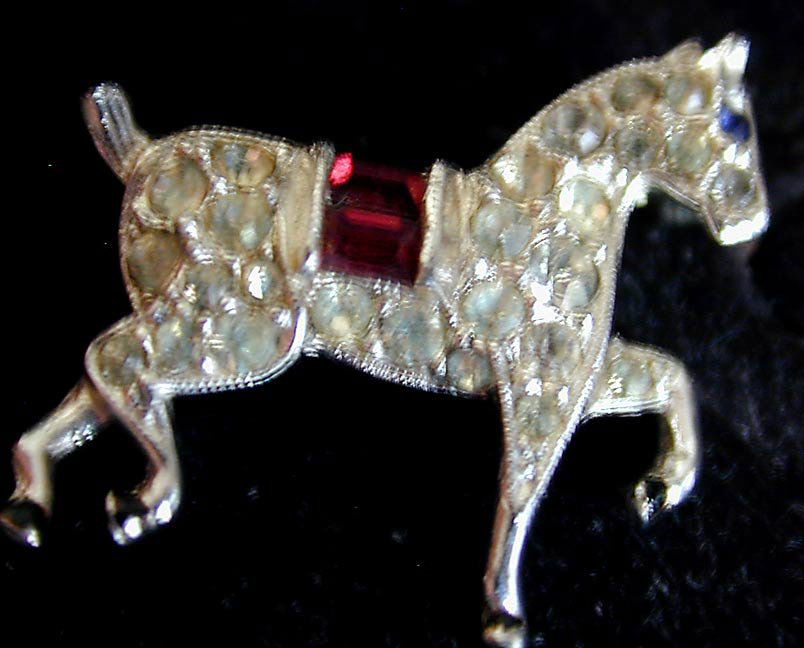 CROWN TRIFARI PRANCING PONY HORSE PIN: A scatter pin of a prancing pony horse; body of horse with clear stones and red stone saddle set in a rhodium plated body; reverse with crowned Trifari mark; 1"L.
