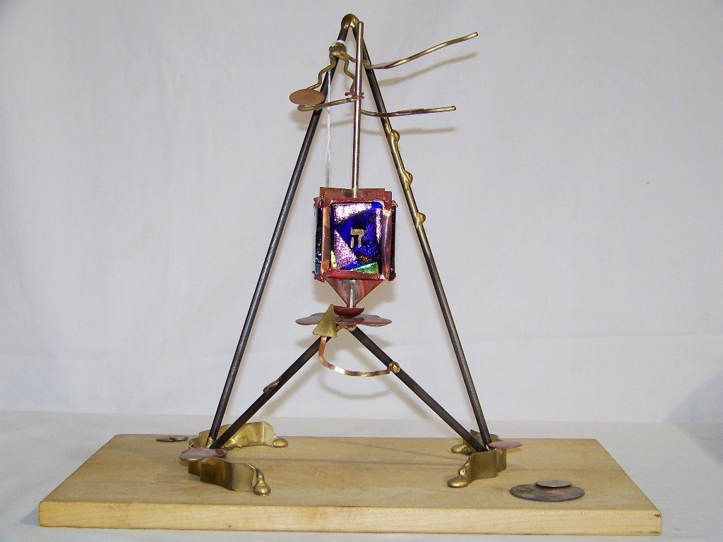 GARY ROSENTHAL GLASS FUSED DREIDEL SCULPTURE: GLASS AND FUSED METAL GARY ROSENTHAL DESK TOP ROTATING DREIDEL.Great sculpture hand made with a wooden base.Signed on metal tag on base.Stands app.14" tall,9 1/2" wide and 6 1/2" deep.Wood base is 9 3