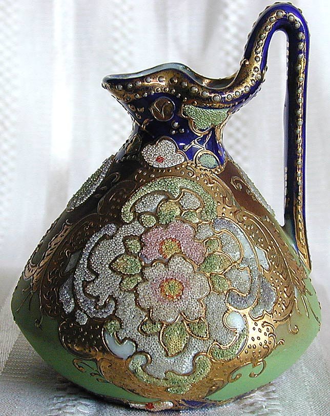 Nippon Porcelain Coralene Ewer 4"H: Nippon circa 1910 heavily gilt with floral beaded cartouche and royal blue painted handle, 4" high with some missing beading.No chips, cracks or repairs