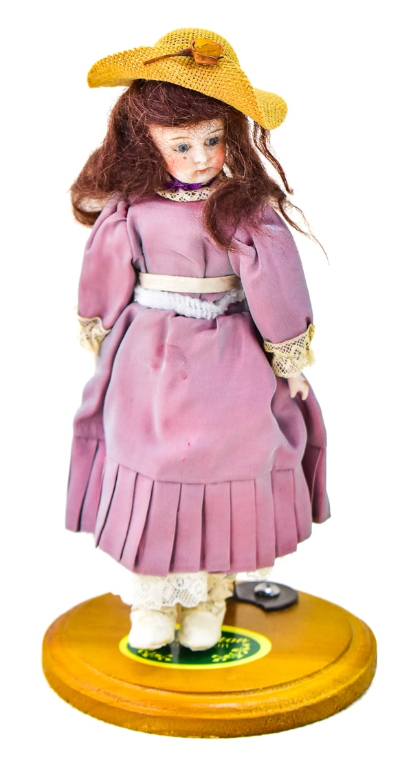 ANTIQUE GERMAN GIRL DOLL WITH PURPLE DRESS: Antique German girl doll with purple dress and straw brimmed hat. Measures 8" tall.