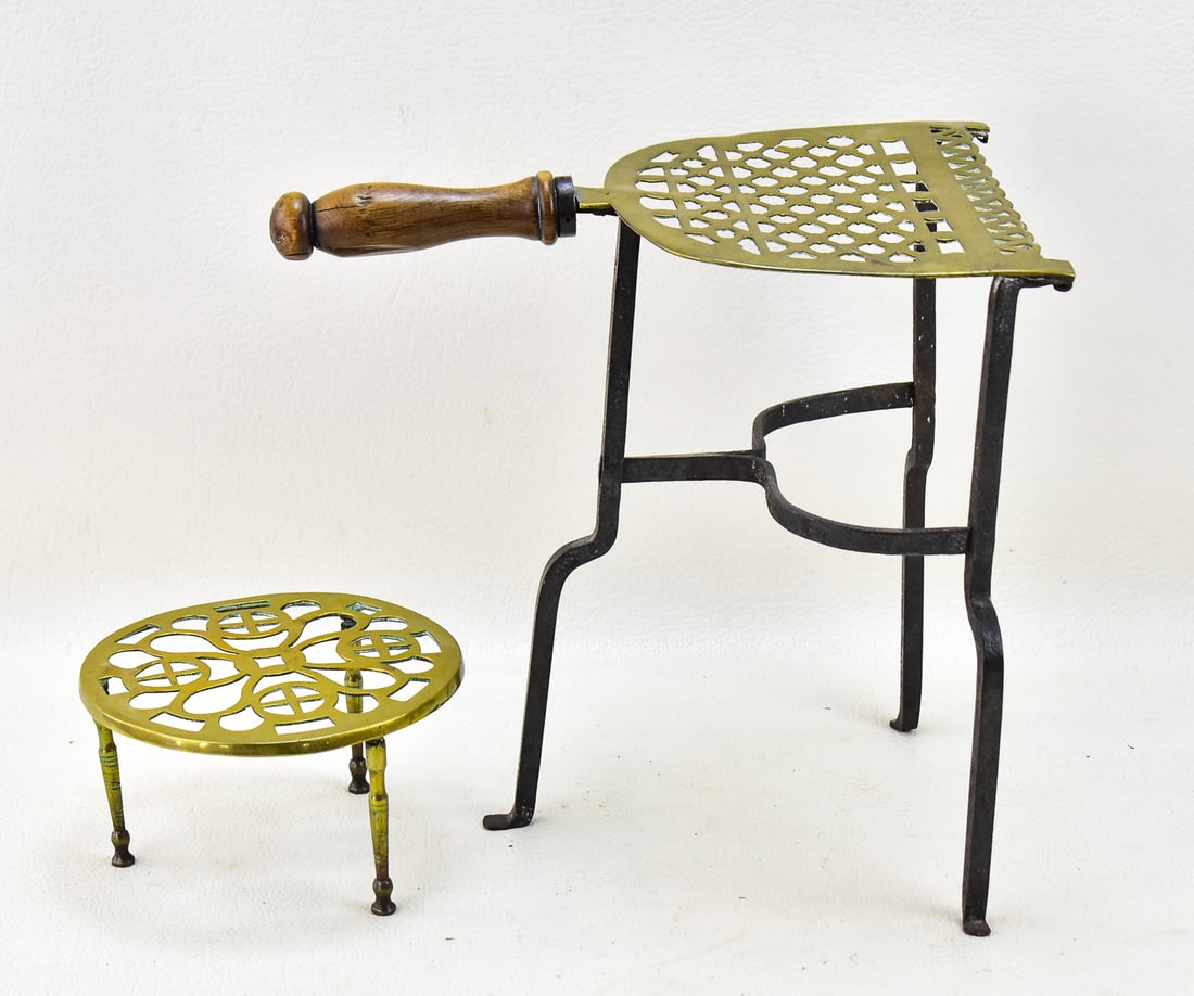 PAIR OF BRASS TRIVETS: A pair of brass trivets, one of which is quite tall with wrought-iron feet and a wooden handle.