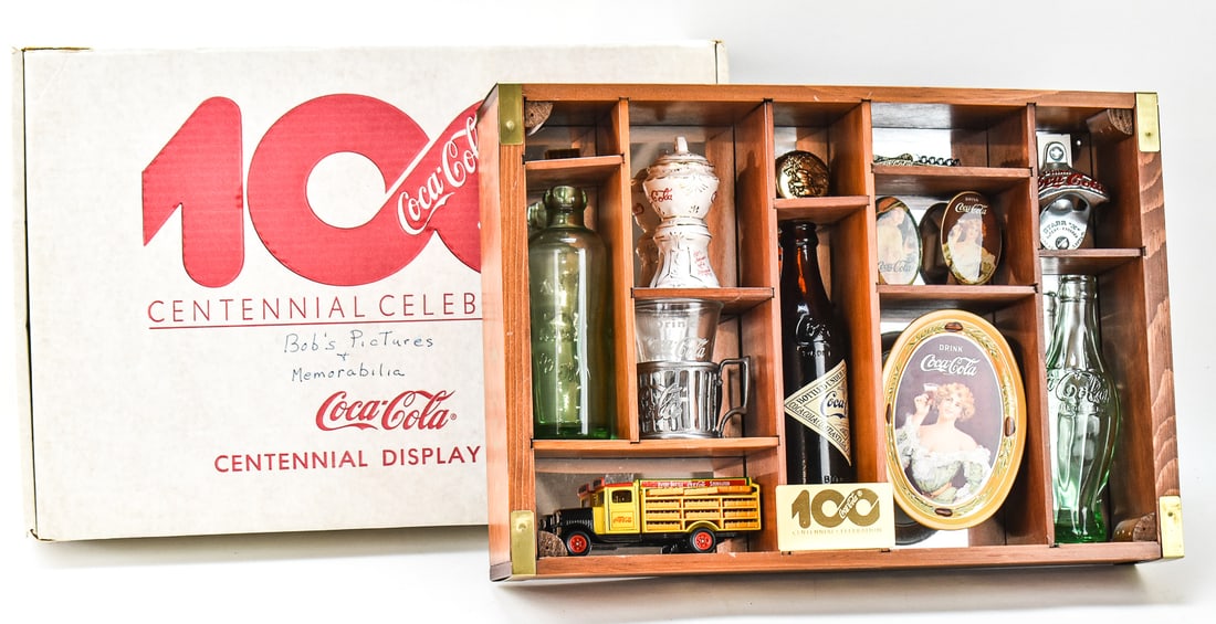 1985 COCA-COLA CENTENNIAL DISPLAY CASE: A 1985 Coca-Cola centennial display case with miniature decorative product icons with the original box. The box measures 4" heigh, 20" wide, and 13.5" deep.