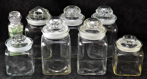 EIGHT GLASS VINTAGE LIDDED CANDY JARS: This lot includes seven glass candy jars and one glass cylinder jar, circa early-mid 20th century. The lot measures 8.5" H x 9.5" W x 19" D.