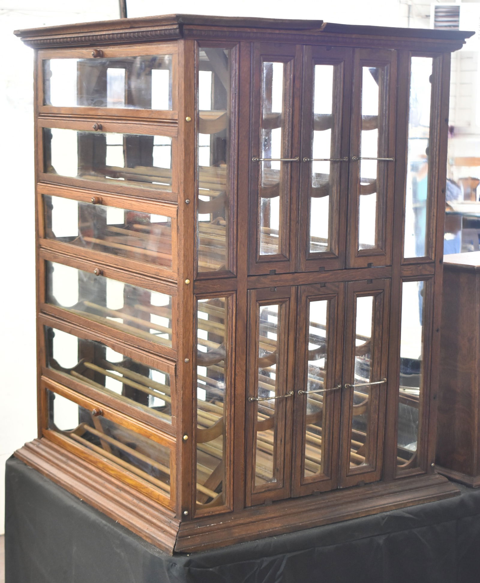 OAK DOUBLE-SIDED RIBBON CABINET, C. EARLY 1900s: An oak double-sided ribbon cabinet with egg and dart trim, six folding doors, and six drawers with three shelves capable of holding wine bottles, circa early 1900s. The item measures 38" H.