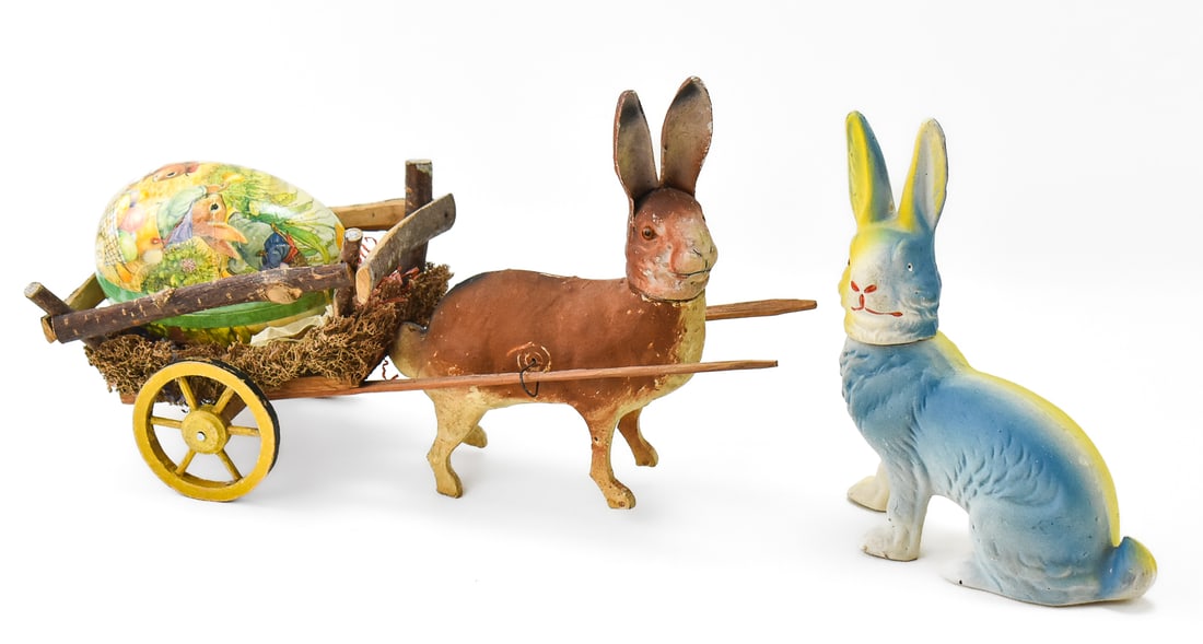 EARLY 20TH C. EASTER BUNNY COMPOSITION DECORATIONS: A pair of early 20th century Easter bunny rabbit decorations, including one pulling an egg cart and another sitting, made of composition or composite paper and wood materials. The rabbit cart display
